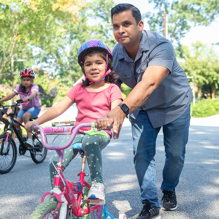 man helping little girl learn to ride a bike