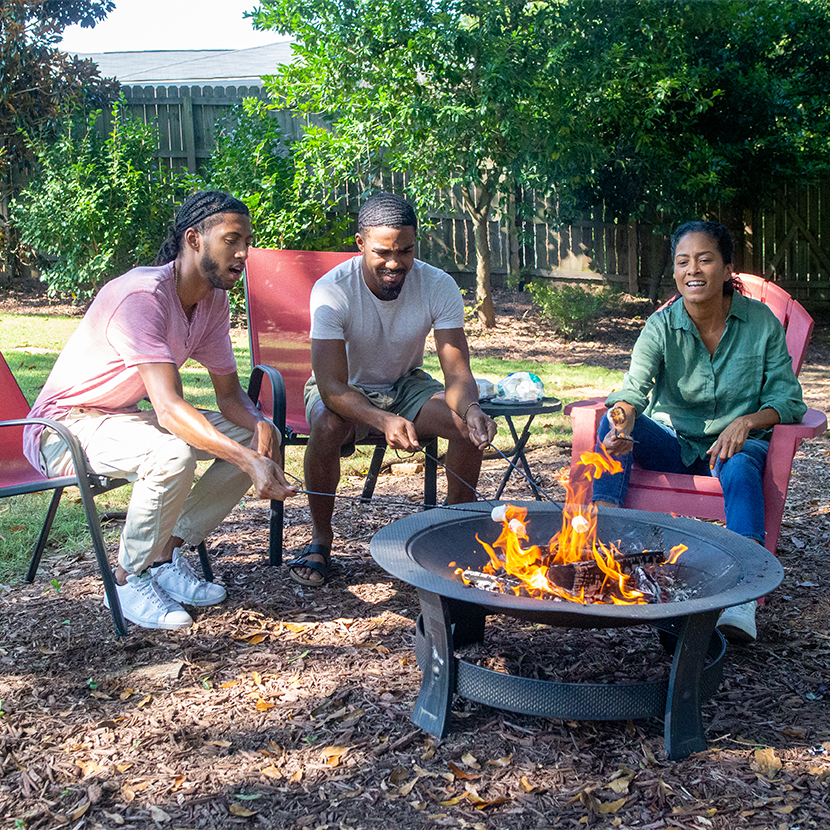 Three smiling young adults sitting around a fire pit considering buying life insurance in the future. 