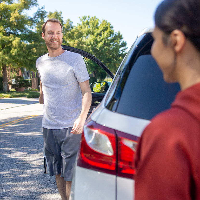 A man talking to a woman outside of his car with his car door open