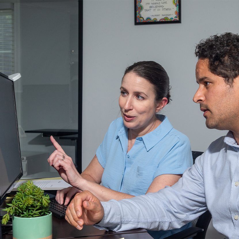 Woman and man sitting at a desk, looking at a computer screen
