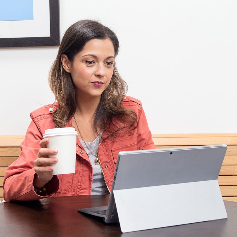 A woman looking at her tablet while holding a coffee cup