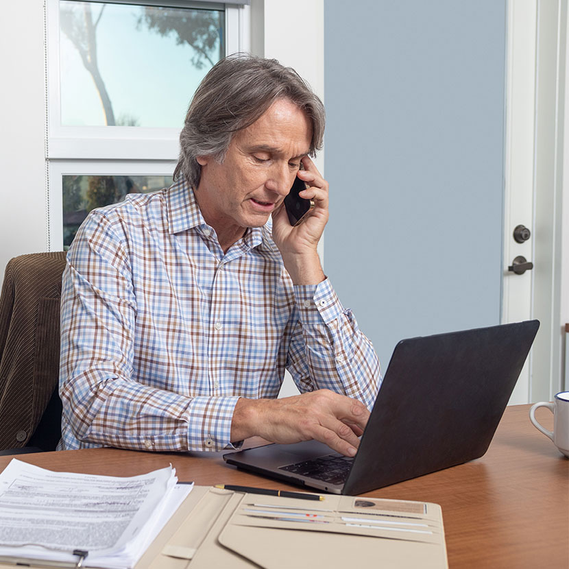 A man reading about TruStage Business Protection resources on his laptop while talking on the phone