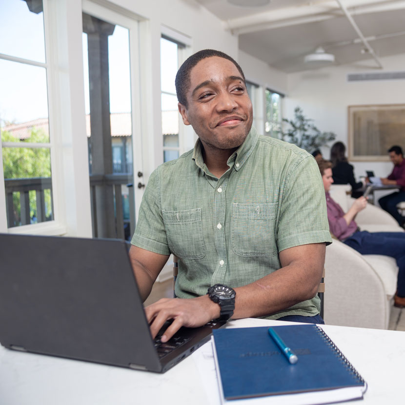 A man smiles while learning about the TruStage Discovery Conference on his laptop