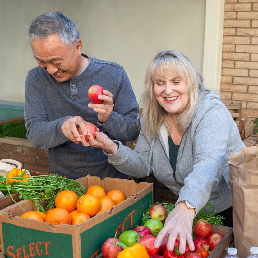 Two TruStage customers smile while picking out fresh produce