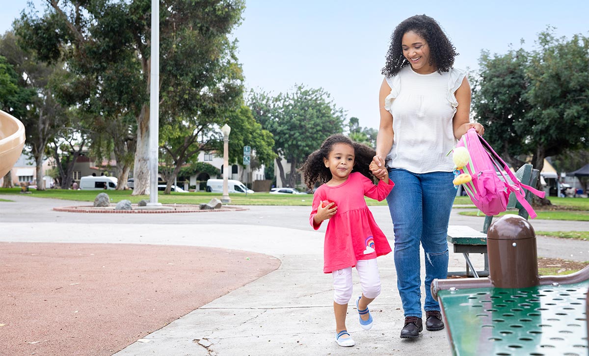 A smiling mother and young daughter protected with TruStage Life Insurance hold hands while walking outside.