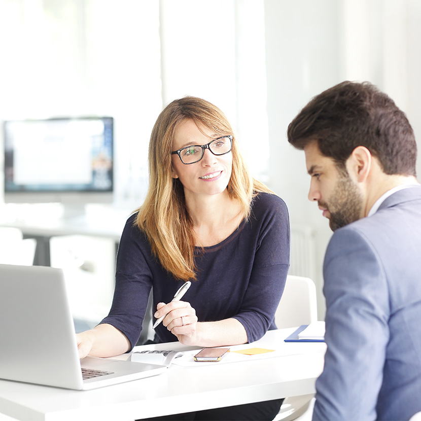 A woman and a man sitting at a table looking at a laptop together