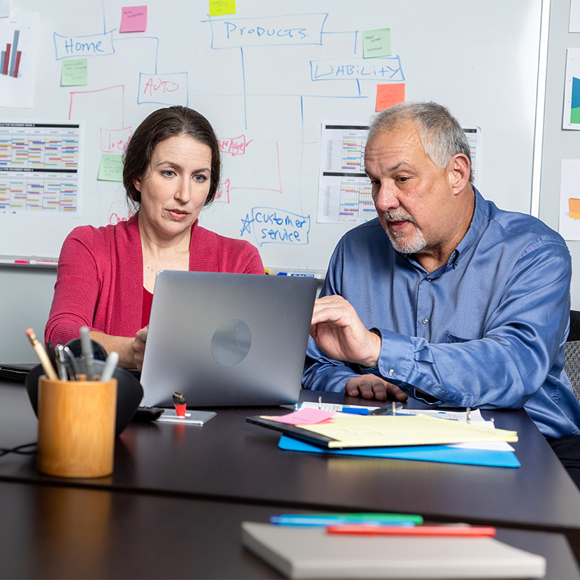 A man and woman working at a table with a laptop and various papers