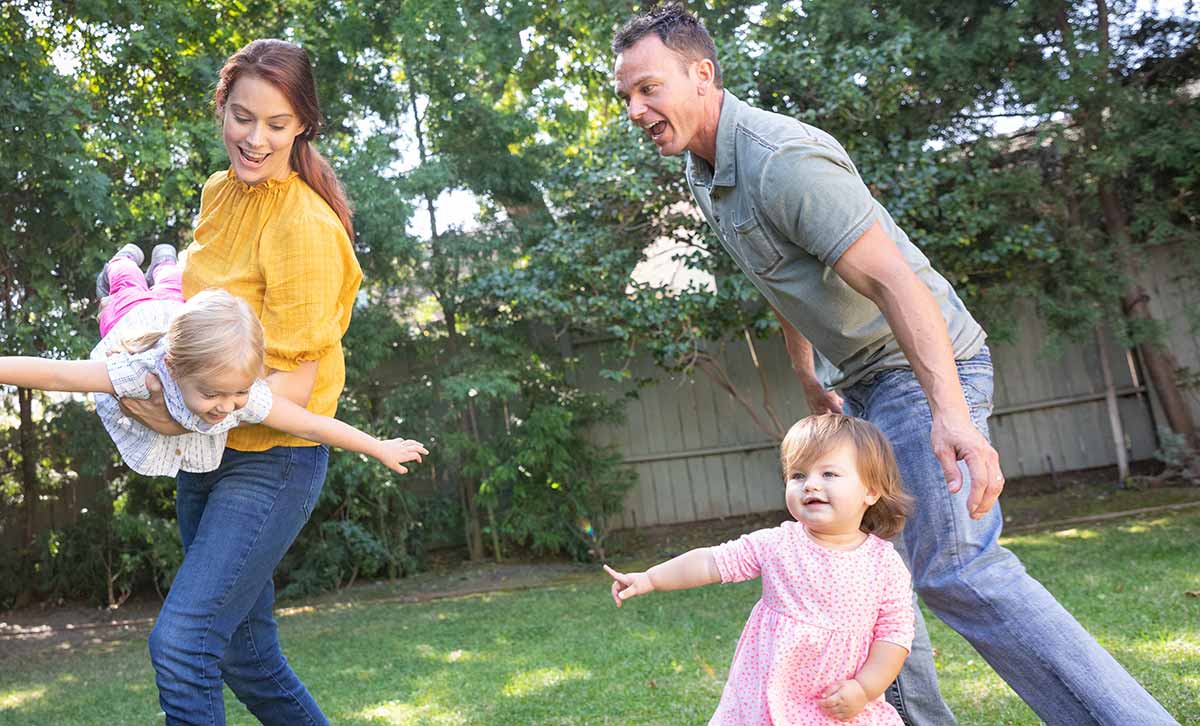 A husband and wife protected with TruStage life insurance play in their yard with their two young daughters.