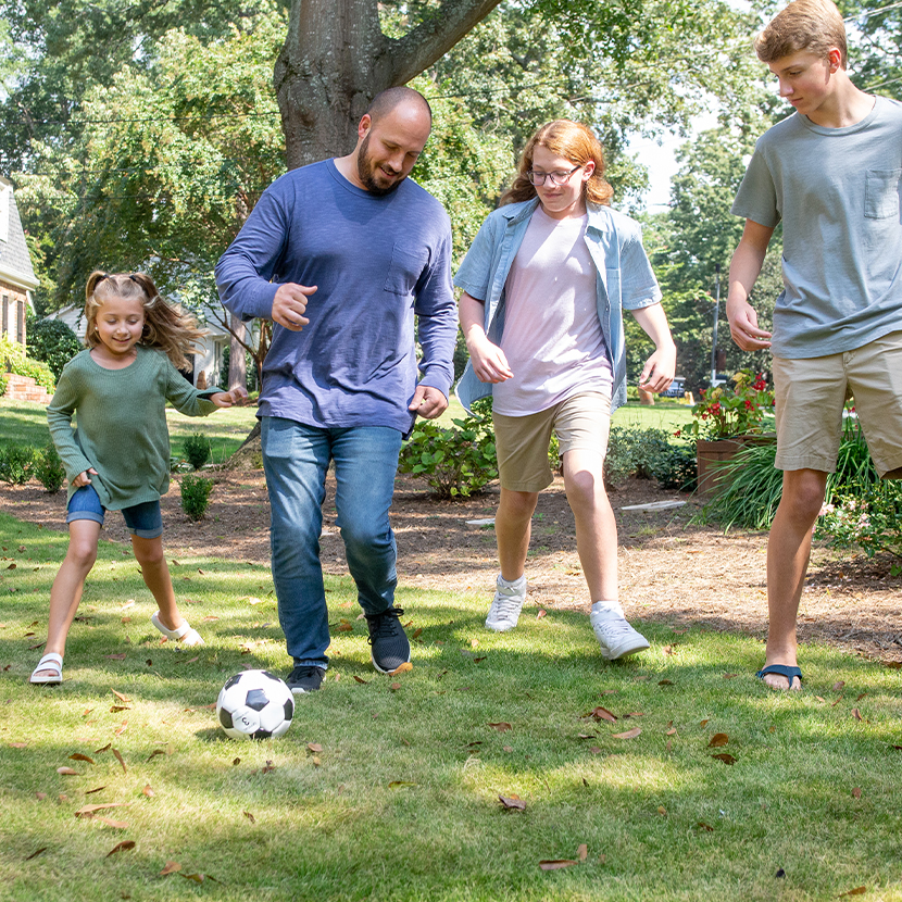 A family of four playing soccer together outside