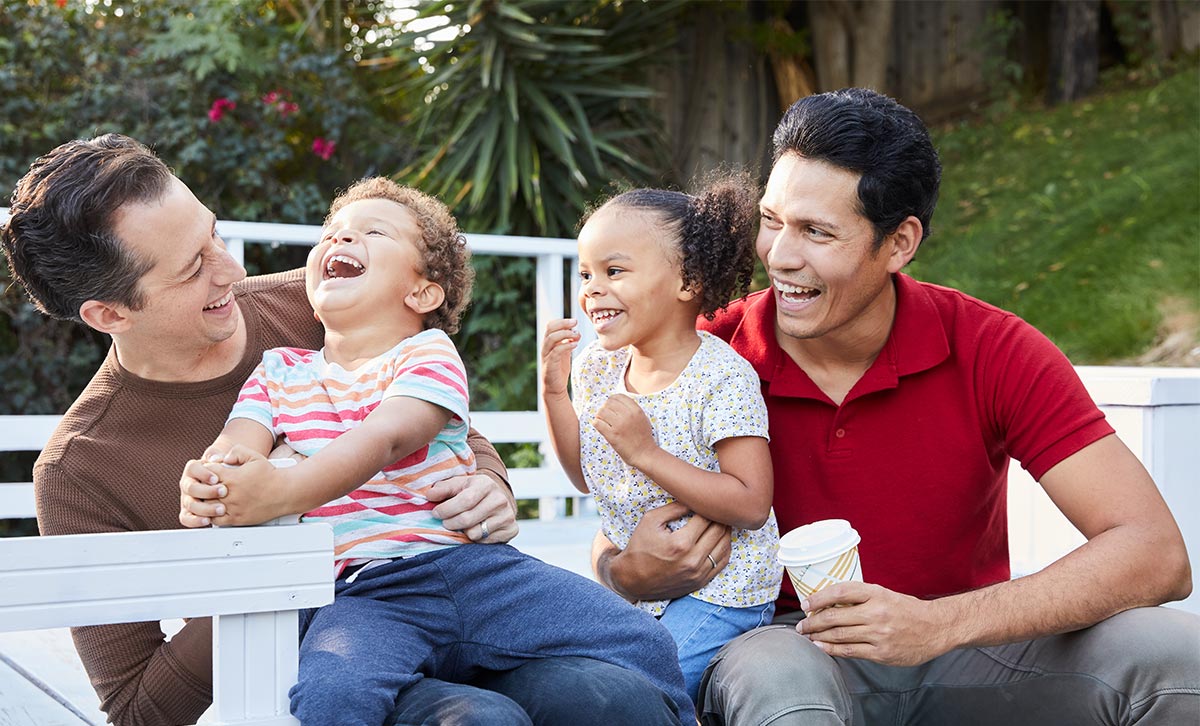 A male couple and their two young children sit in a park feeling thankful for their TruStage life insurance.