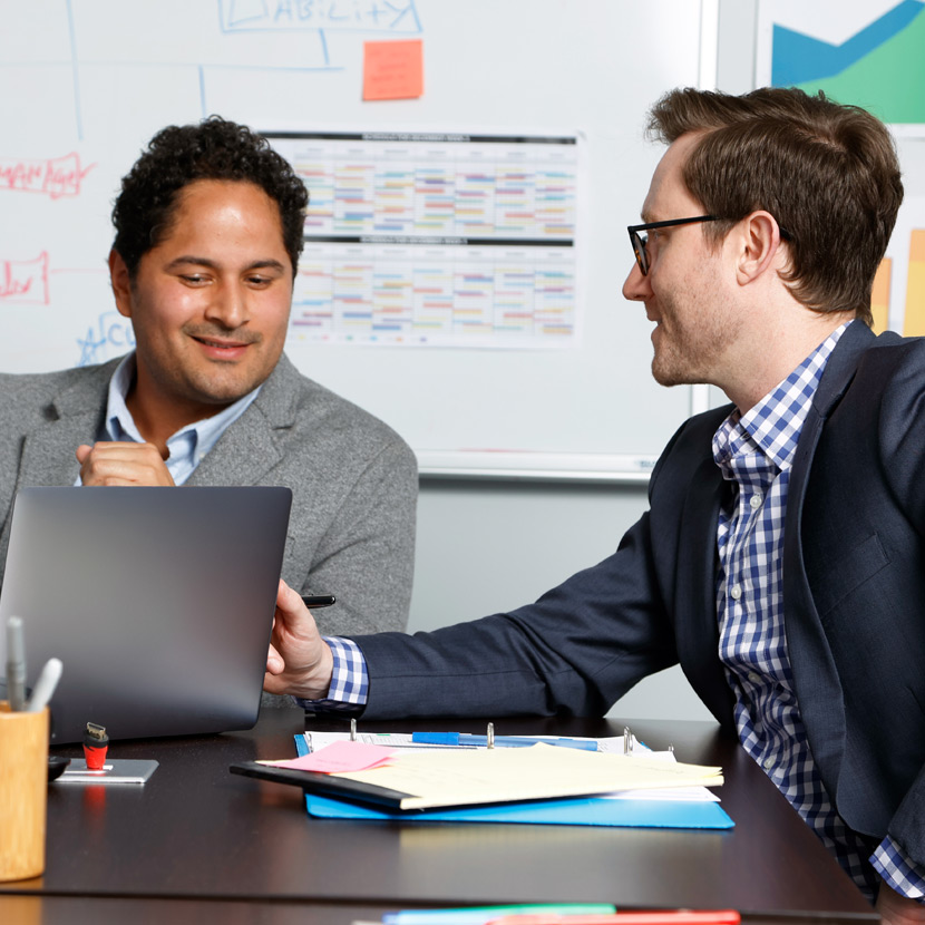 Two smiling men meeting at an office table reviewing insurance reports.