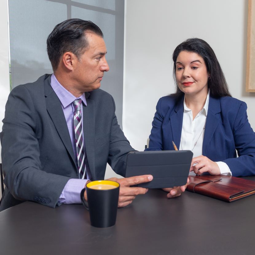 Two financial professionals sit at a desk and review a regulatory tracking tool on a laptop.
