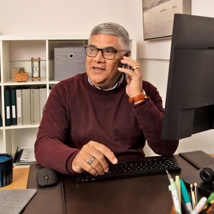 A man sits at a desk and talks on his phone.