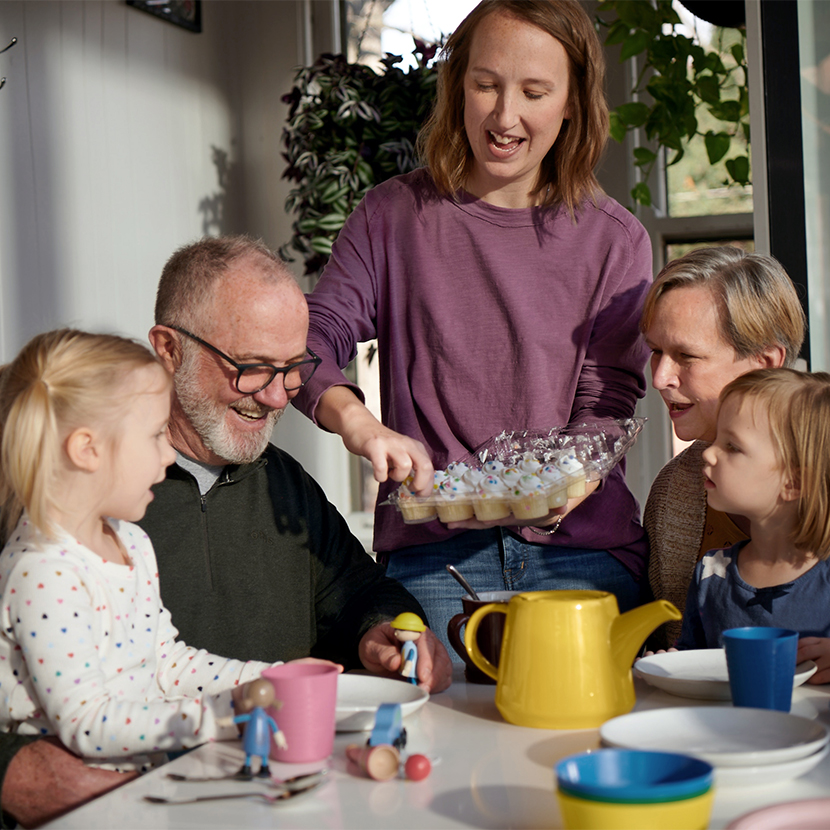 A family sits at a table together while the mom hands out mini cupcakes