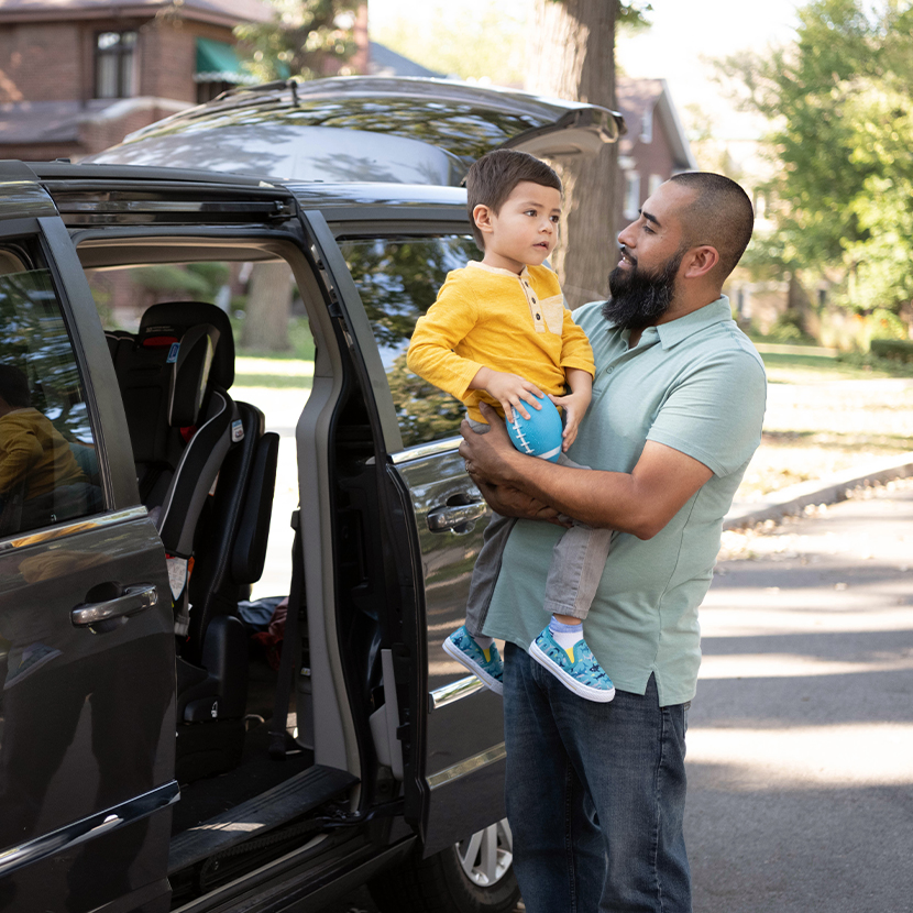 A father holding is son next to a minivan with the back doors open