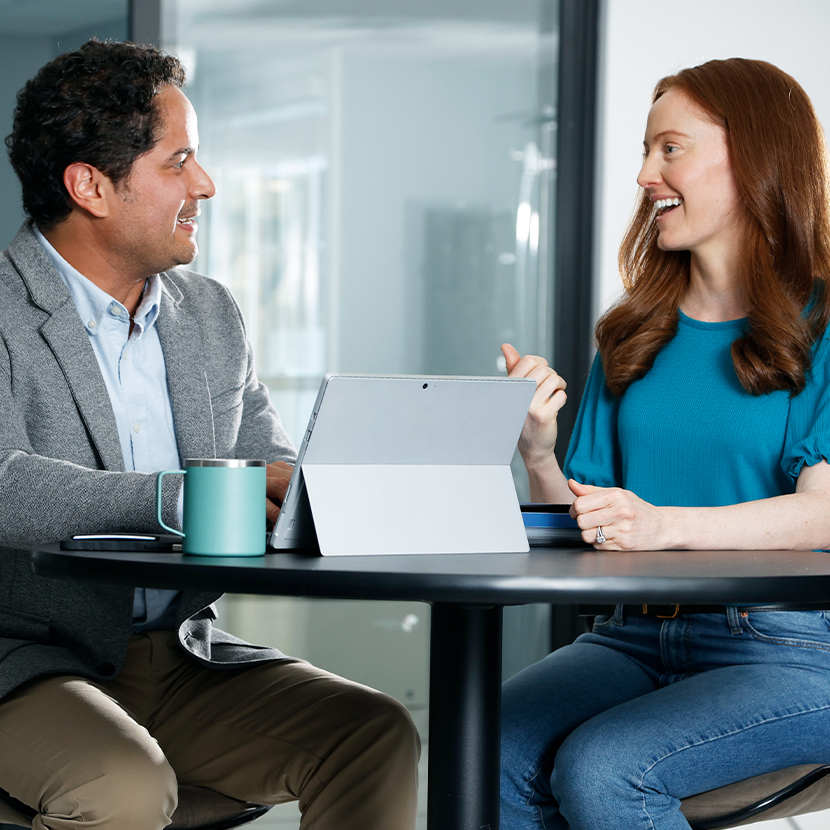 Man and woman sitting at a table, talking, with a tablet open on the table