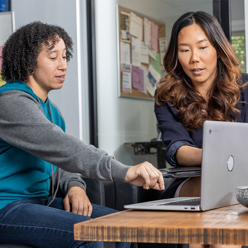 Two women at a laptop discuss a financial plan, made possible by the CRCU and TruStage partnership