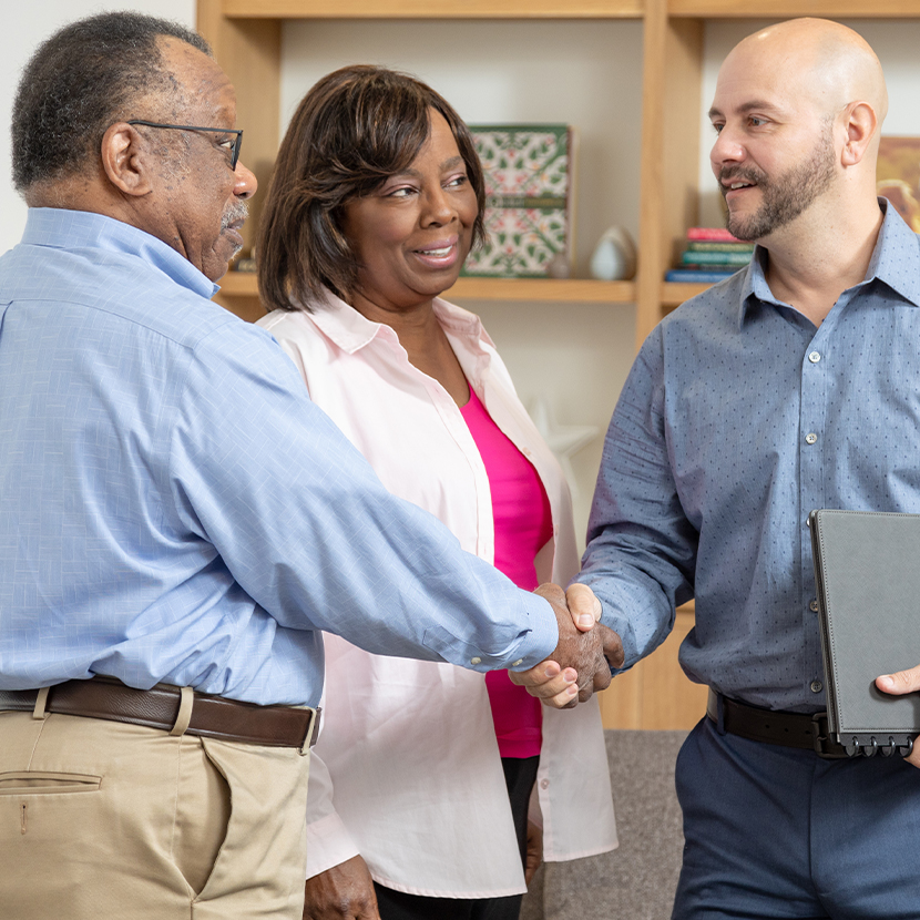 Two men shaking hands, with woman watching and smiling