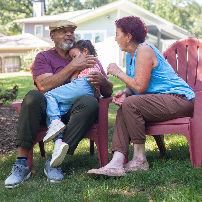 Grandparents sitting in patio chairs hugging grandchild