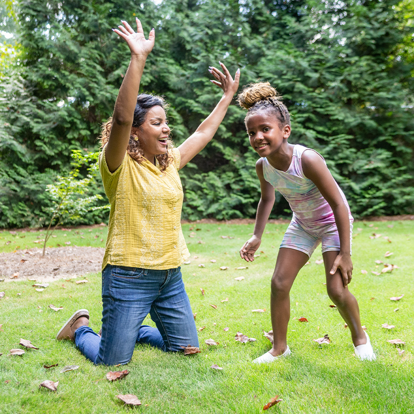 A mom kneeling playing with her daughter outside on the grass