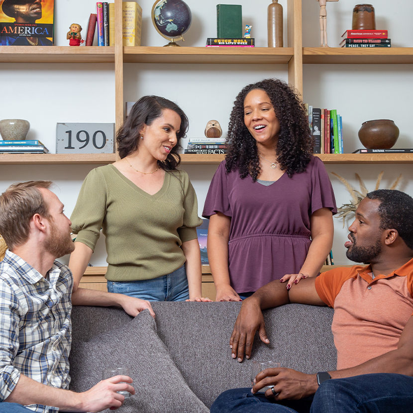 Two men sitting on a couch with two women standing behind the couch