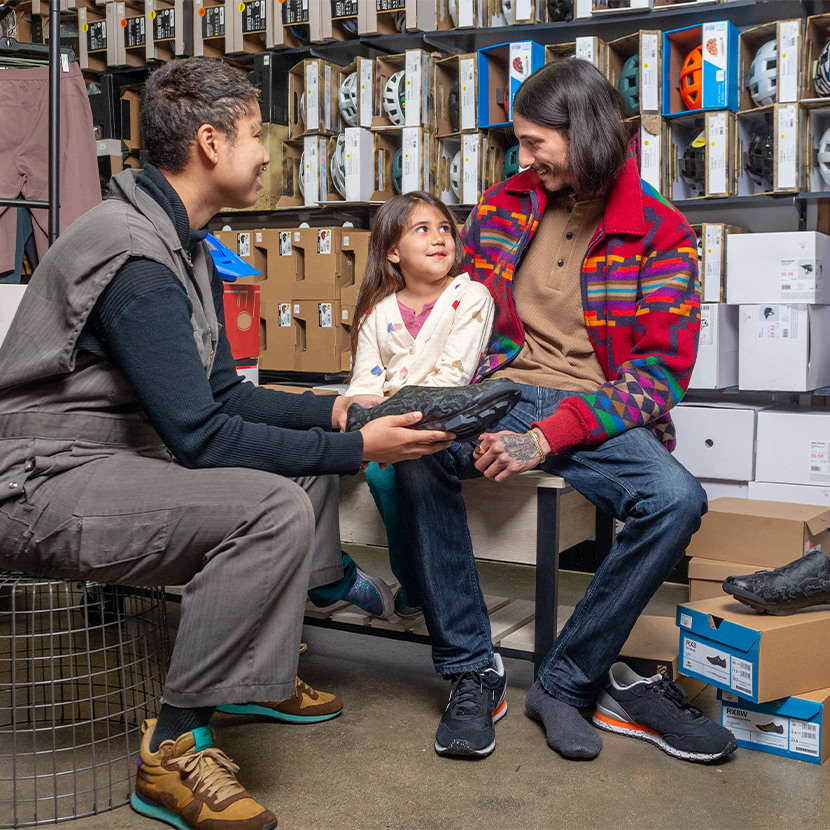 Father sits next to her daughter in a shoe store while an employee shows them a shoe