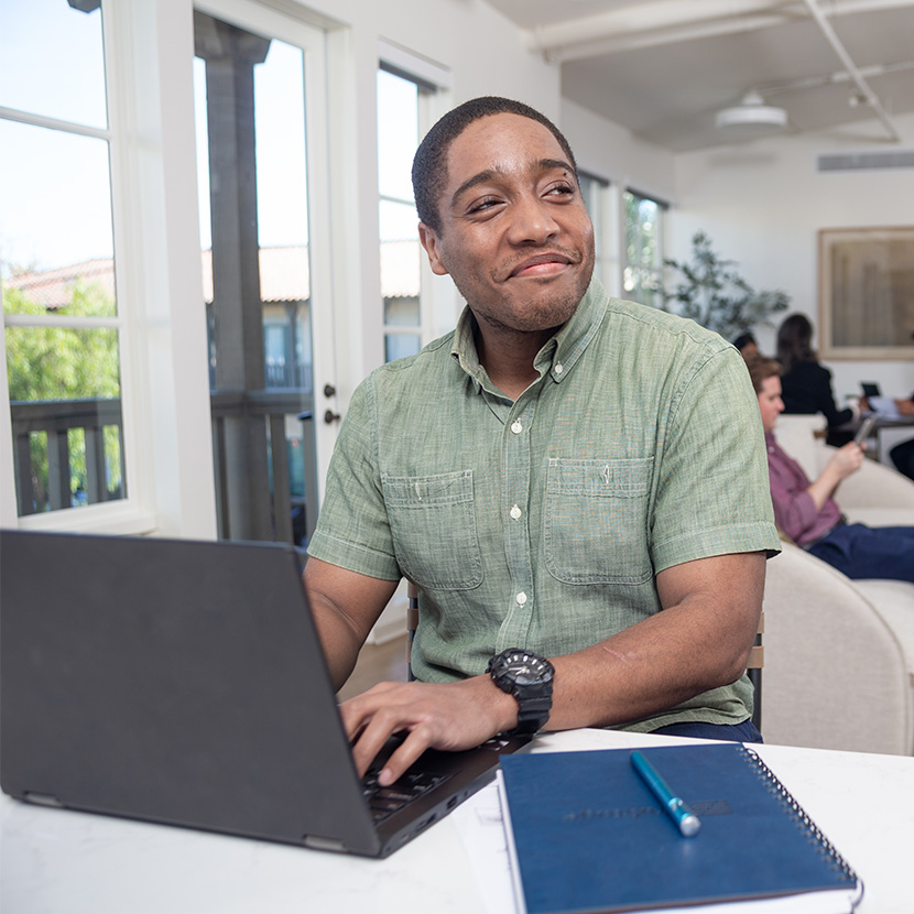 A man smiles while sitting at his laptop, proud that TruStage Payment Guard Insurance won gold in the Best in Biz Awards.