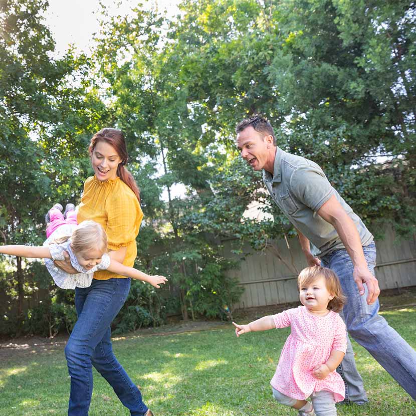 A husband and wife protected with TruStage life insurance play in their yard with their two young daughters.