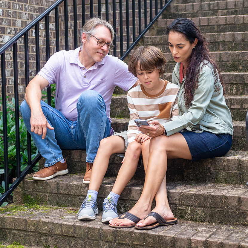 Father, mother and son use a smartphone and TruStage’s Behavioral Finance Advice program to improve financial decision-making.