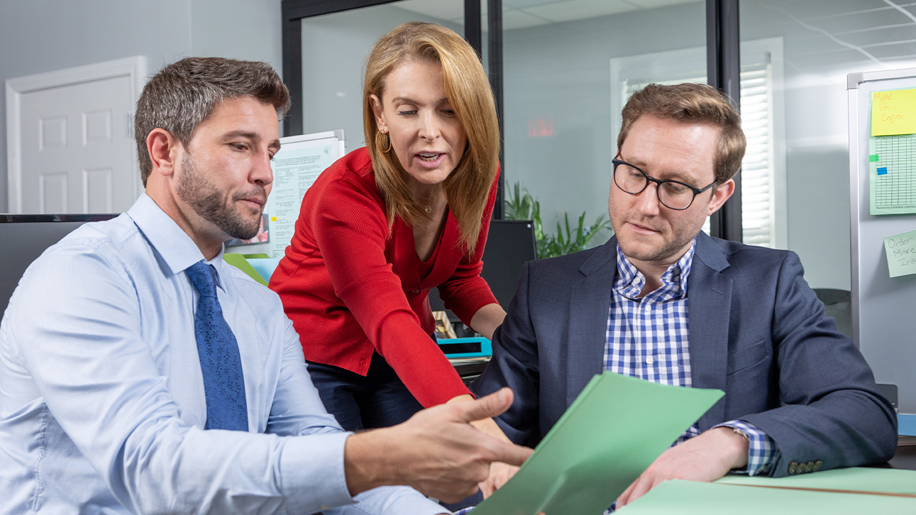 A woman and two men in an office, looking at a piece of paper and pointing to it