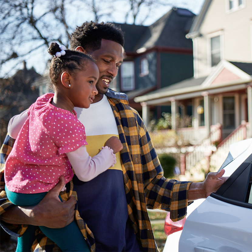 Man opening the back door of a car while holding a young girl