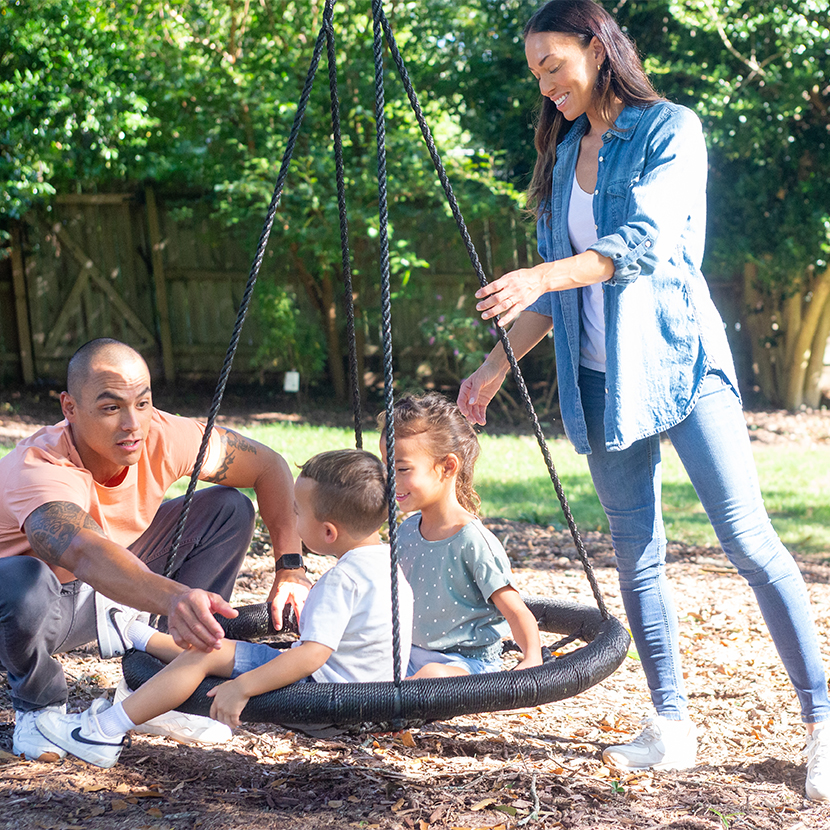 Man and a woman pushing two young kids on a swing outside