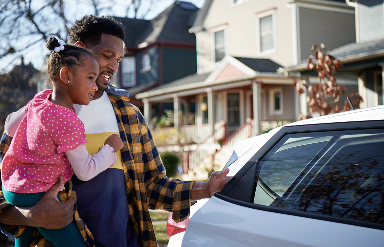 Man opening the back door of a car while holding a young girl