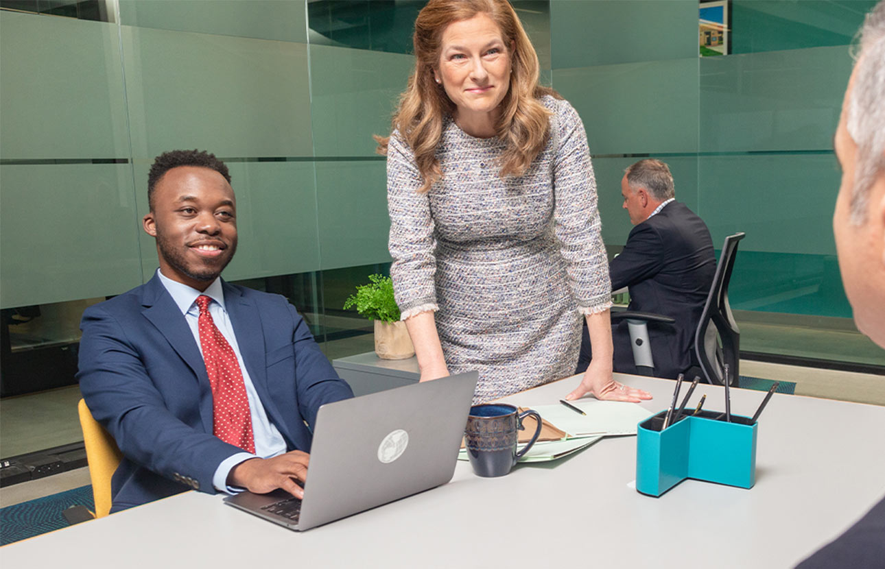 A woman and a man in an office setting at a table, looking at a man across the table from them