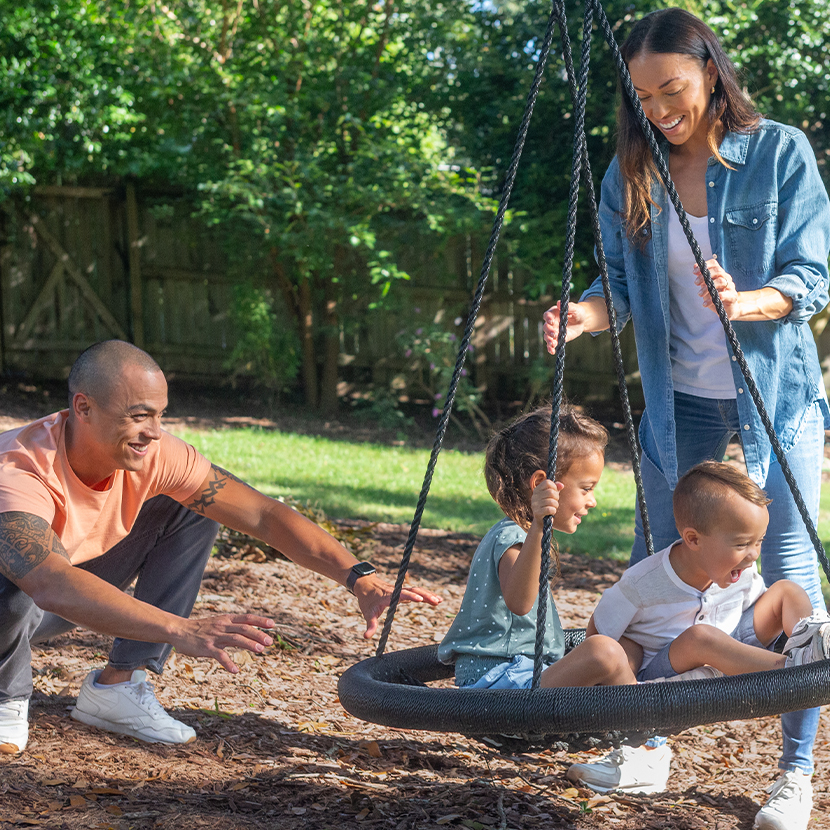 Man and woman pushing two young children on a swing, outside