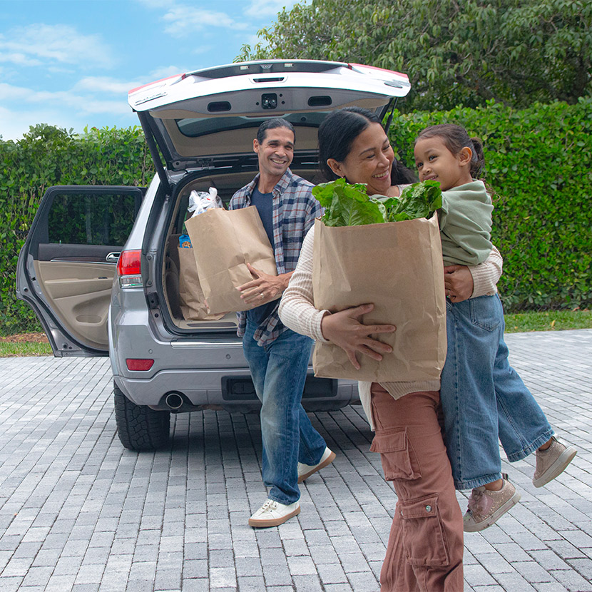 Parents with their young daughter unload groceries from their car that is protected with extended auto care.