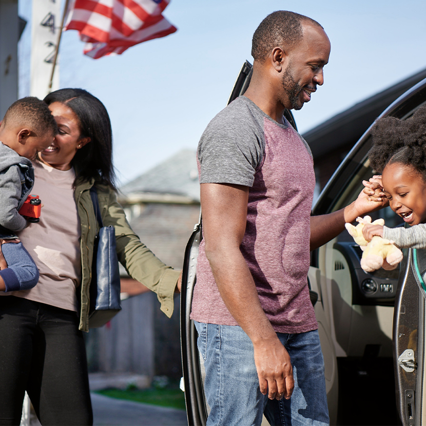 Man, woman and two young children all outside, by a vehicle with open doors