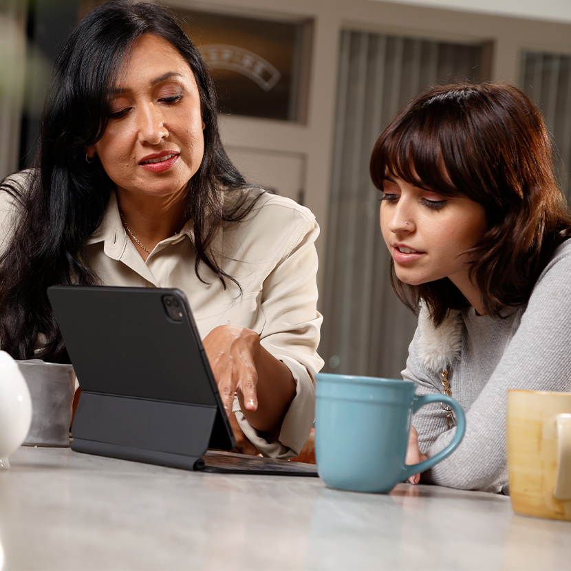 Woman and an adolescent female sitting at a table, looking at a tablet