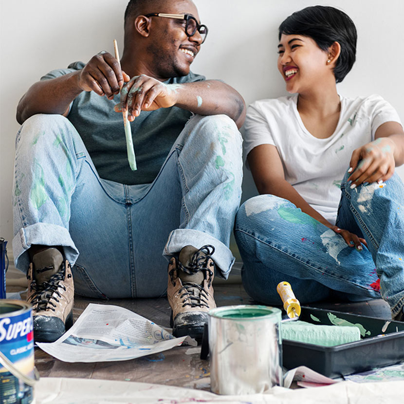 Man and woman sitting on the ground, surrounded by paint supplies