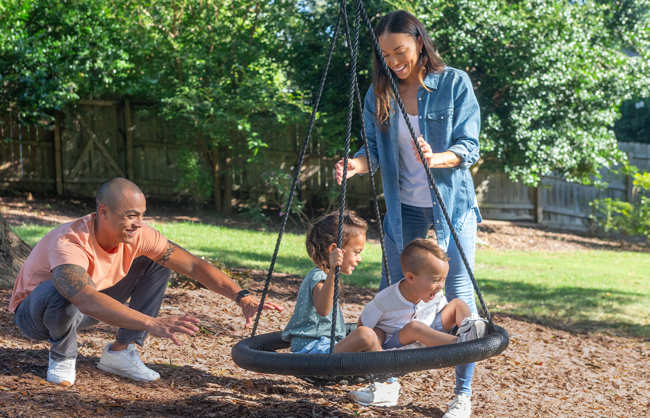 Man and woman that have prepared for the unexpected with debt protection push two young children outside on a swing 