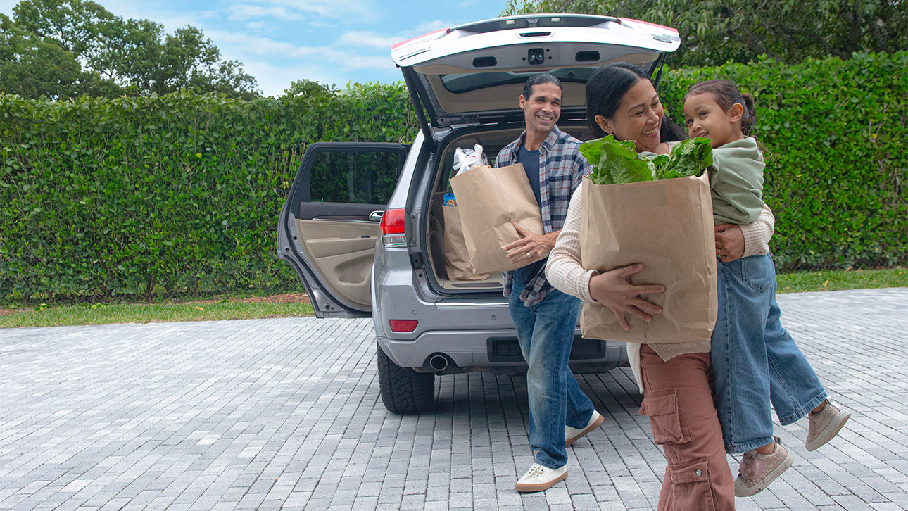 Parents with their young daughter unload groceries from their car that is protected with extended auto care.   