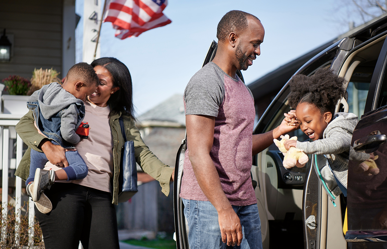 Man, woman and two young children all outside, by a vehicle with open doors