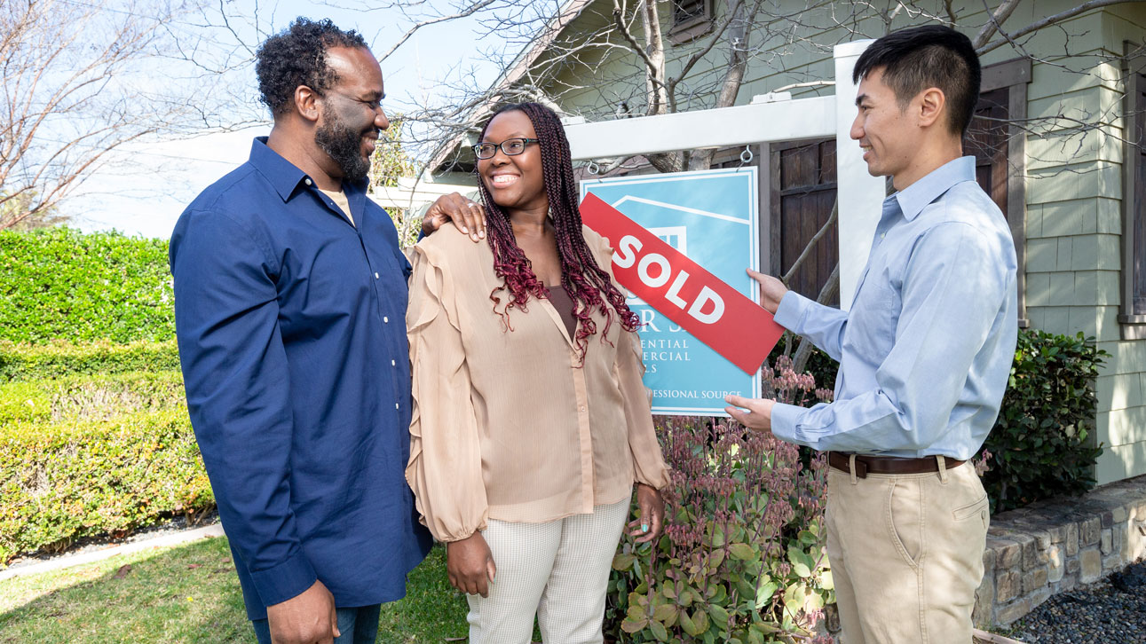 A couple stands by the sold sign of their new house, thanks to TruStage private mortgage insurance