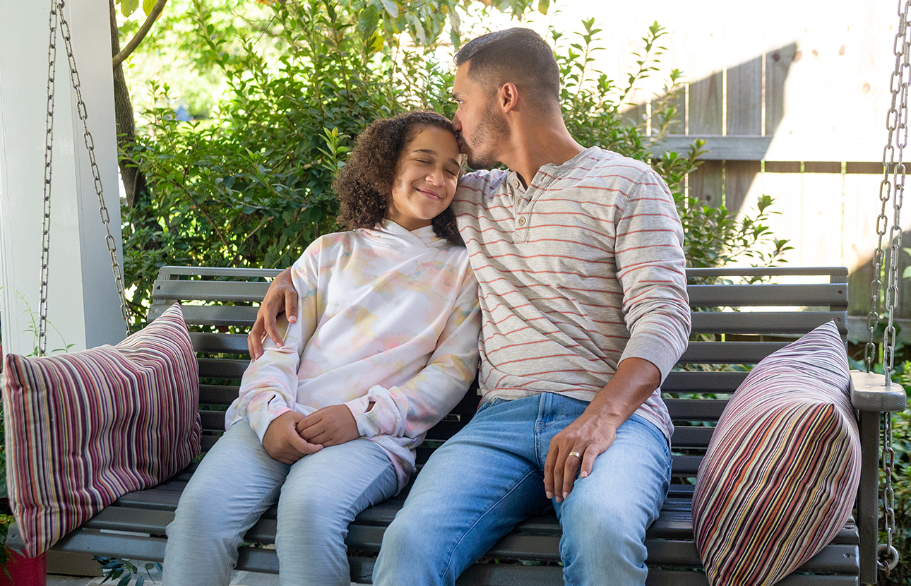 Man and adolescent female sitting on a swing outside, man kissing female on the forehead