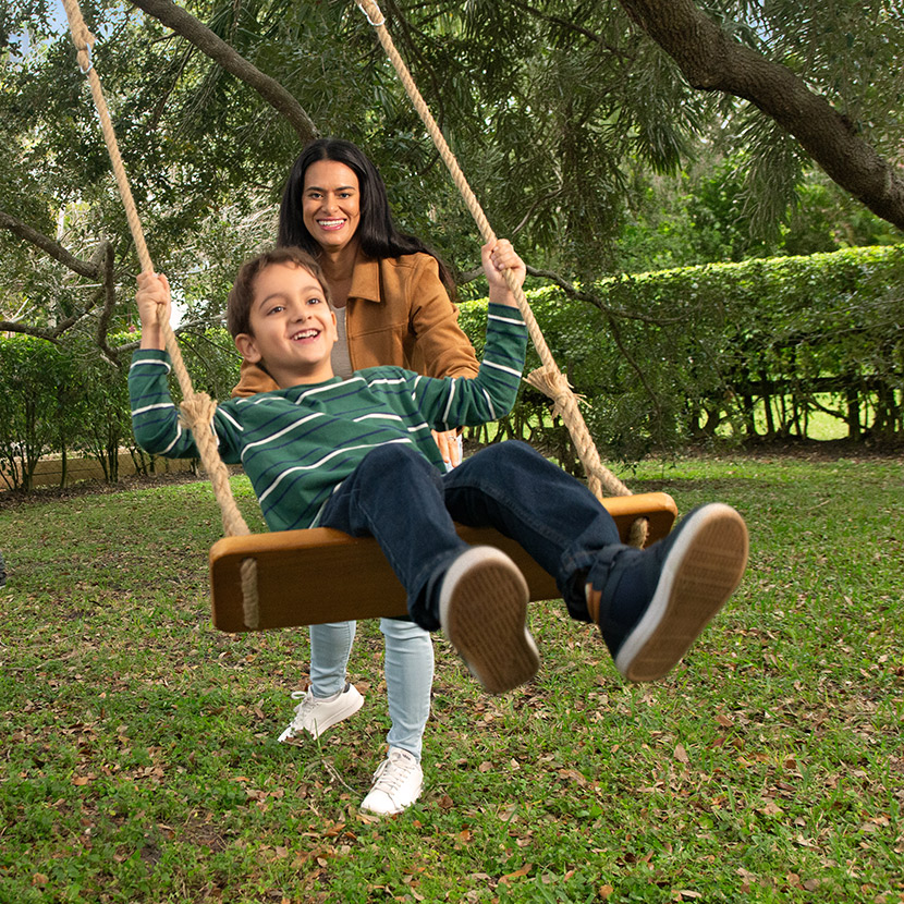  A mother pushes her son on a swing while a father plays soccer with his children in the backyard.
