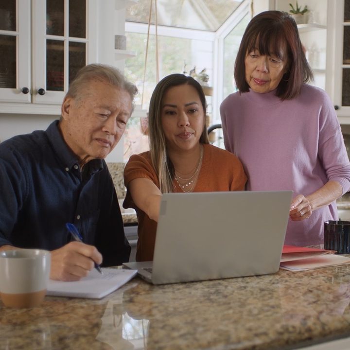 A woman sits at a laptop with her parents by her side as she applies for a life insurance policy.