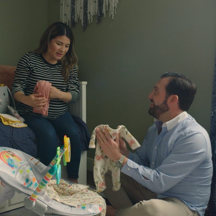 A husband and wife discuss life insurance riders while organizing a child's room.