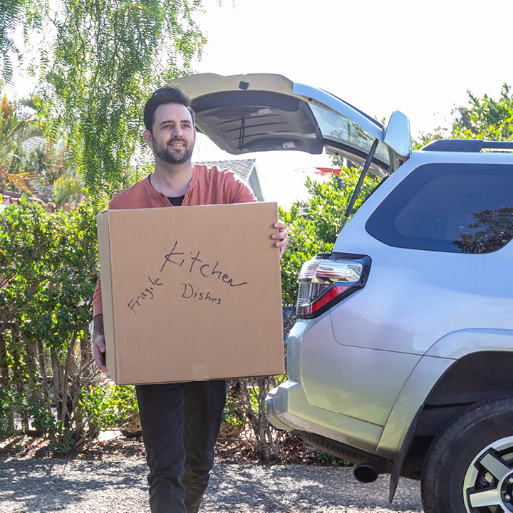 A man carries a box from his vehicle on moving day, feeling protected with mechanical repair coverage.