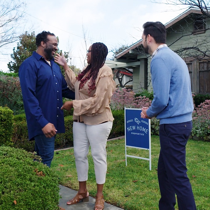 A husband and wife stand with their realtor in front of their new home.