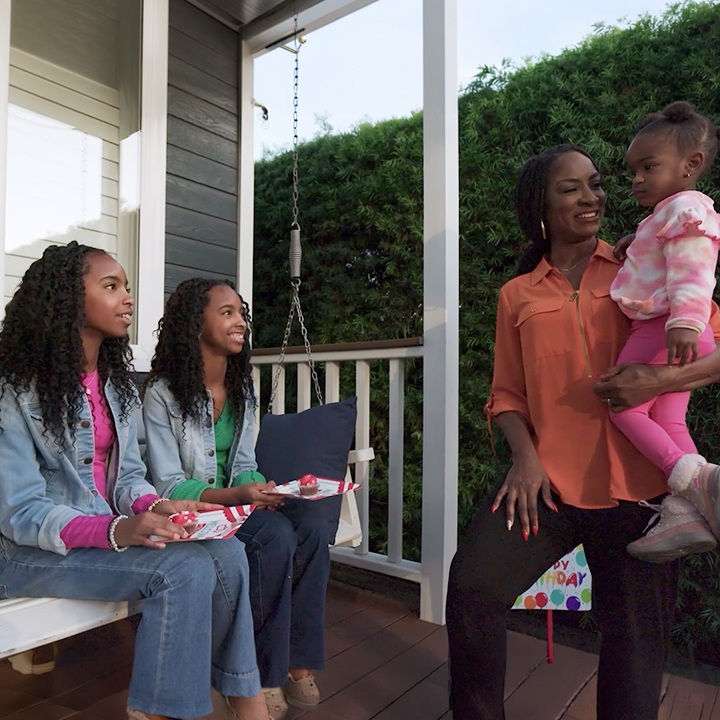 A mother stands on the front porch with her children.